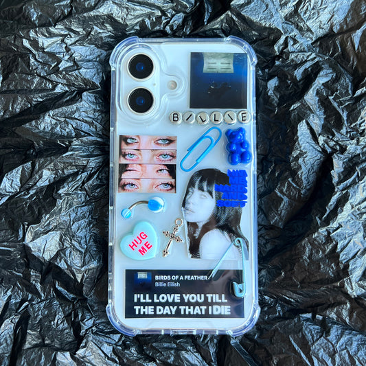 Billie Eilish phone case featuring a collage of blue-themed elements, including a blue paperclip, Birds of a feather lyrics,, blue beads, a blue heart, and a blue photo of a woman, laid flat on a crumpled black background.