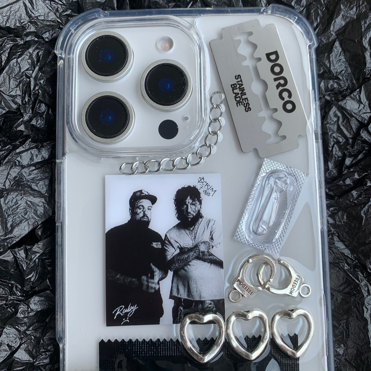 Phone case with various items including a Dorco razor blade, Playboy condoms, and a photo of $uicideboy$ on a crumpled black surface.