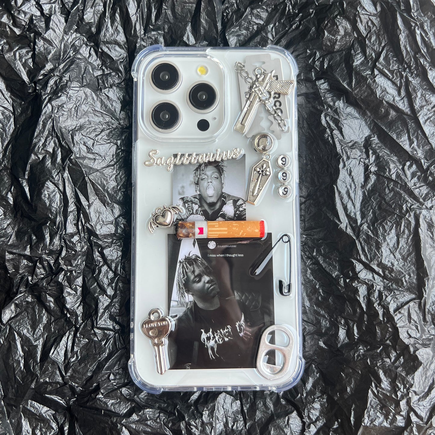 Juice Wrld collage resin custom Phone case featuring a custom graphic collage with black-and-white photos, silver keychains, a small orange item, metallic charms, and the word 'Sagittarius' in script, laid flat on a crumpled black surface.