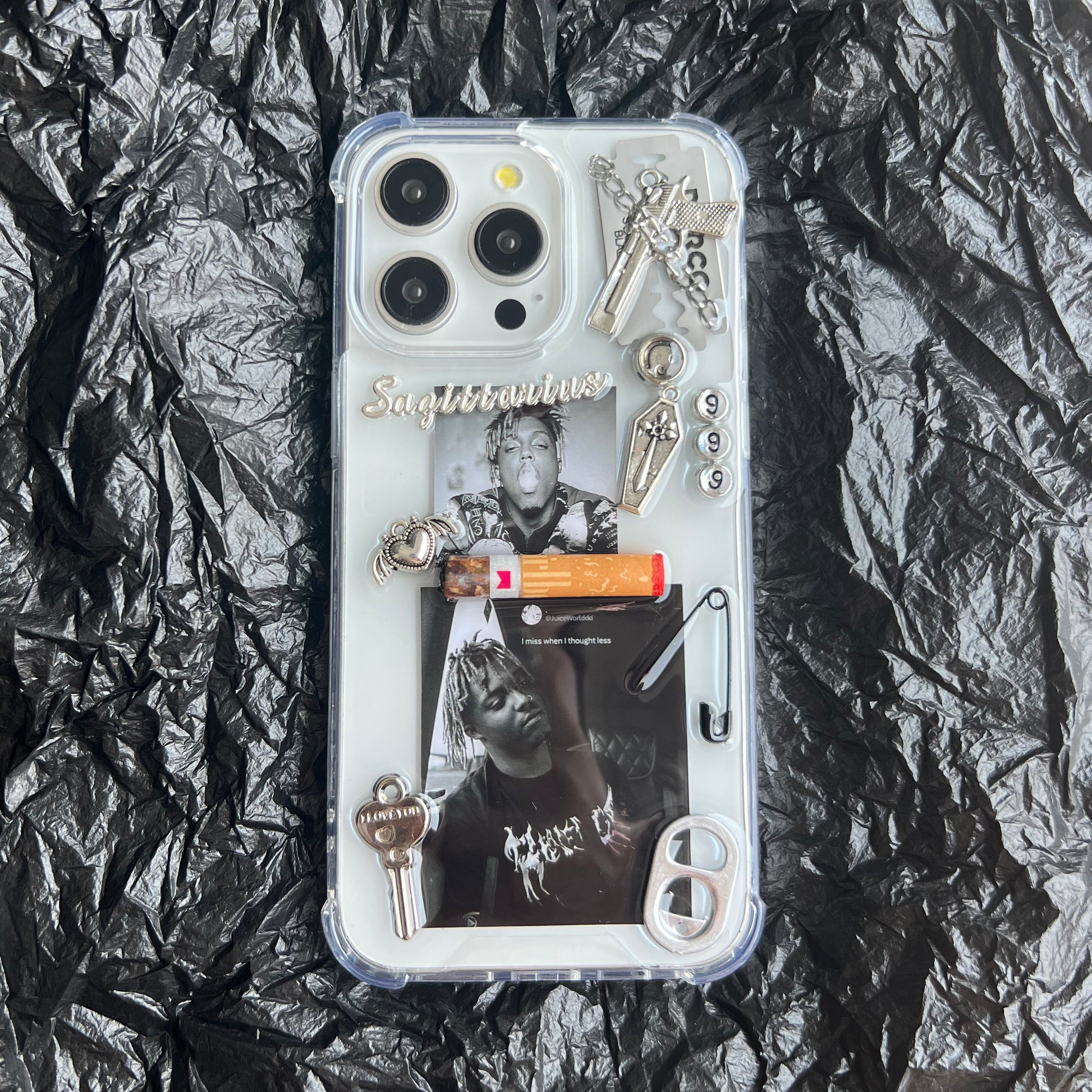 Juice Wrld collage resin custom Phone case featuring a custom graphic collage with black-and-white photos, silver keychains, a small orange item, metallic charms, and the word 'Sagittarius' in script, laid flat on a crumpled black surface.