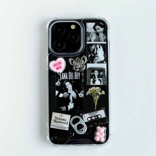lana del rey collage resin custom phone case featuring a black collage design with photos of Lana Del Rey, a pink heart sticker that reads 'HUG ME', a butterfly charm, cassette tape, bottle opener, and small decorative elements, shown on a light gray background.